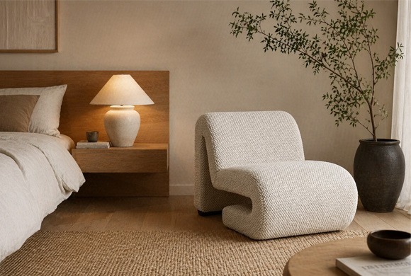 Sillón moderno beige de diseño curvo en dormitorio con muebles de madera y decoración natural Sillón bajo tapizado en tejido beige con diseño curvo en dormitorio moderno con mesilla de madera y lámpara