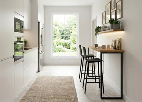 Cocina moderna estrecha con barra alta y dos taburetes Cocina alargada y estrecha de estilo moderno con muebles blancos de suelo a techo, gran ventana al fondo, barra alta de madera junto a la pared y dos taburetes negros, en un espacio luminoso y funcional.