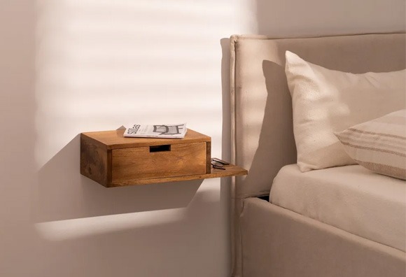 Mesita de noche flotante de madera con diseño compacto y funcional Mesita de noche flotante de madera con cajón junto a cama tapizada en tonos beige